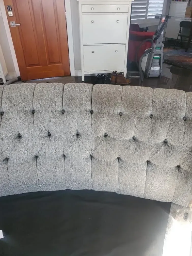 Tufted gray sofa in a living room, with a wooden door and white cabinet in the background