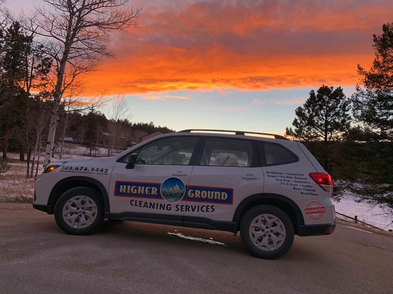 A Higher Ground Cleaning Services SUV parked outdoors during a vibrant orange and purple sunset.