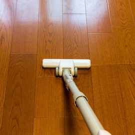 A white vacuum cleaner head moves across polished, light brown wooden floorboards.
