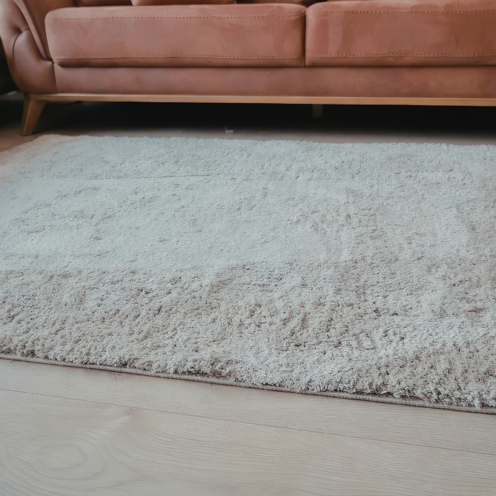 A shaggy, light-colored rug sits on a light wooden floor in front of a modern, rust-colored sofa.