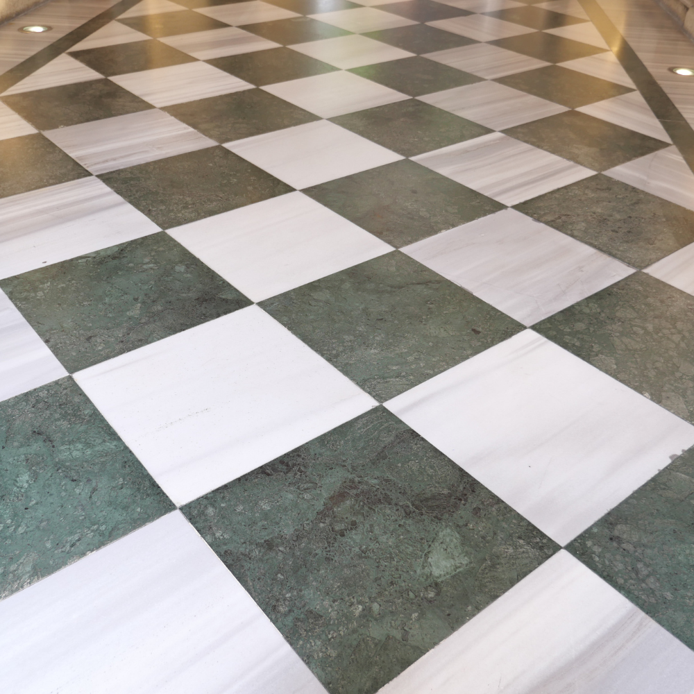 A high-angle view of a checkerboard floor with alternating square tiles in white marble and dark green stone.