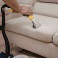 A hand uses an extraction vacuum tool to deep clean a light-colored fabric sofa.