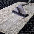 A white rug being cleaned by a professional steam cleaning nozzle on a black, honeycomb-patterned grid surface.