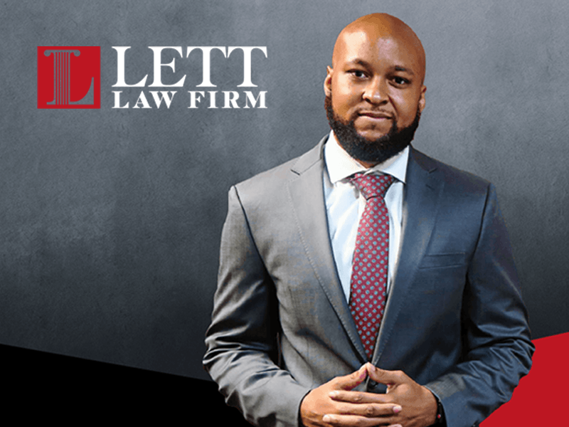 A man in a suit and tie is standing in front of a lett law firm logo