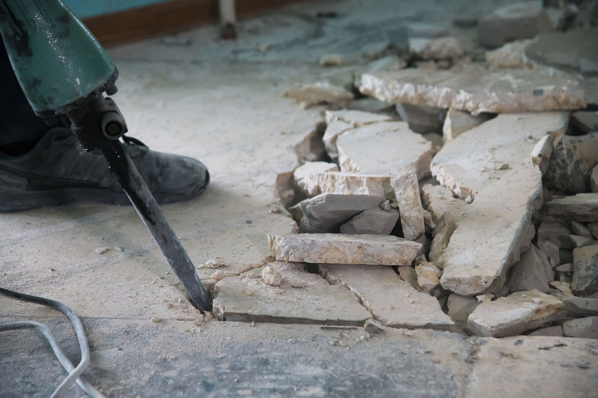 A person is using an equipment to break concrete on the floor.