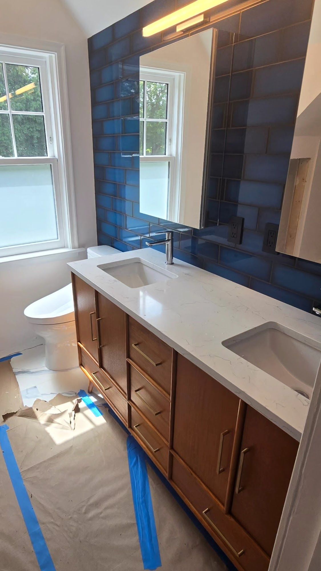 Bathroom with a wooden vanity, white countertop, blue tiled accent wall, and large mirror.