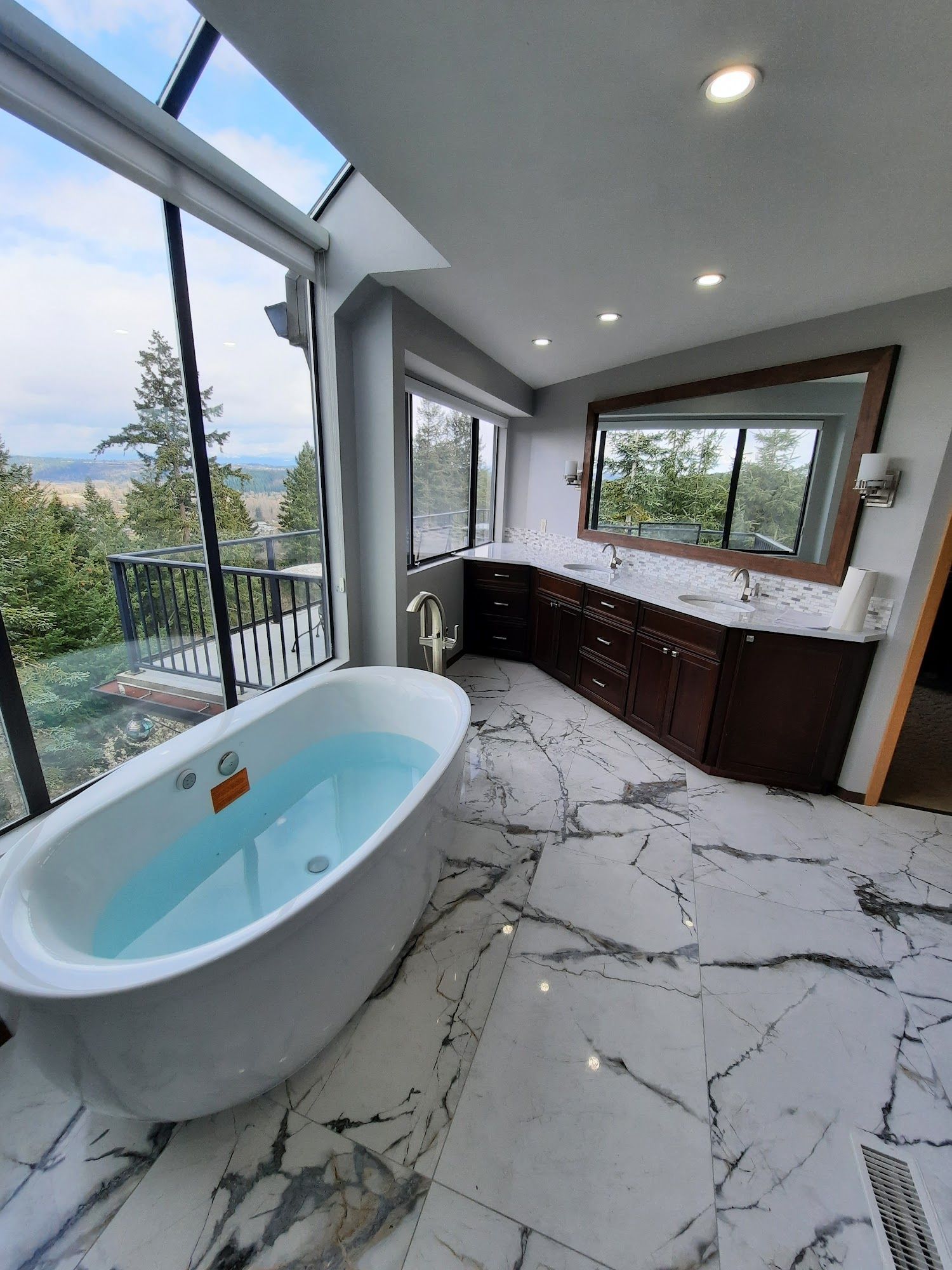 Spacious modern bathroom with a tub, large windows, and a view of trees and hills.