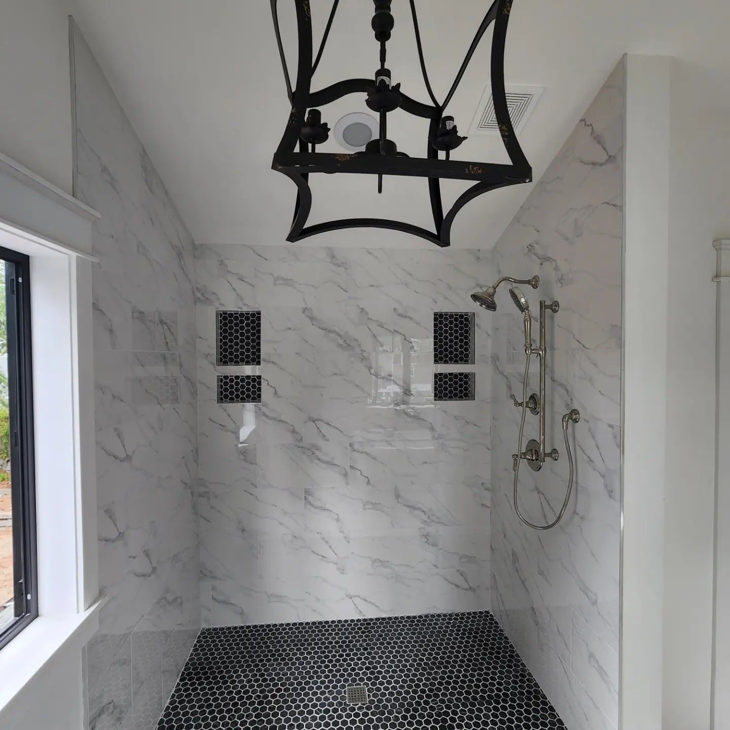 Shower with marble-look tile, black floor tiles, two niche shelves, and a decorative light fixture.