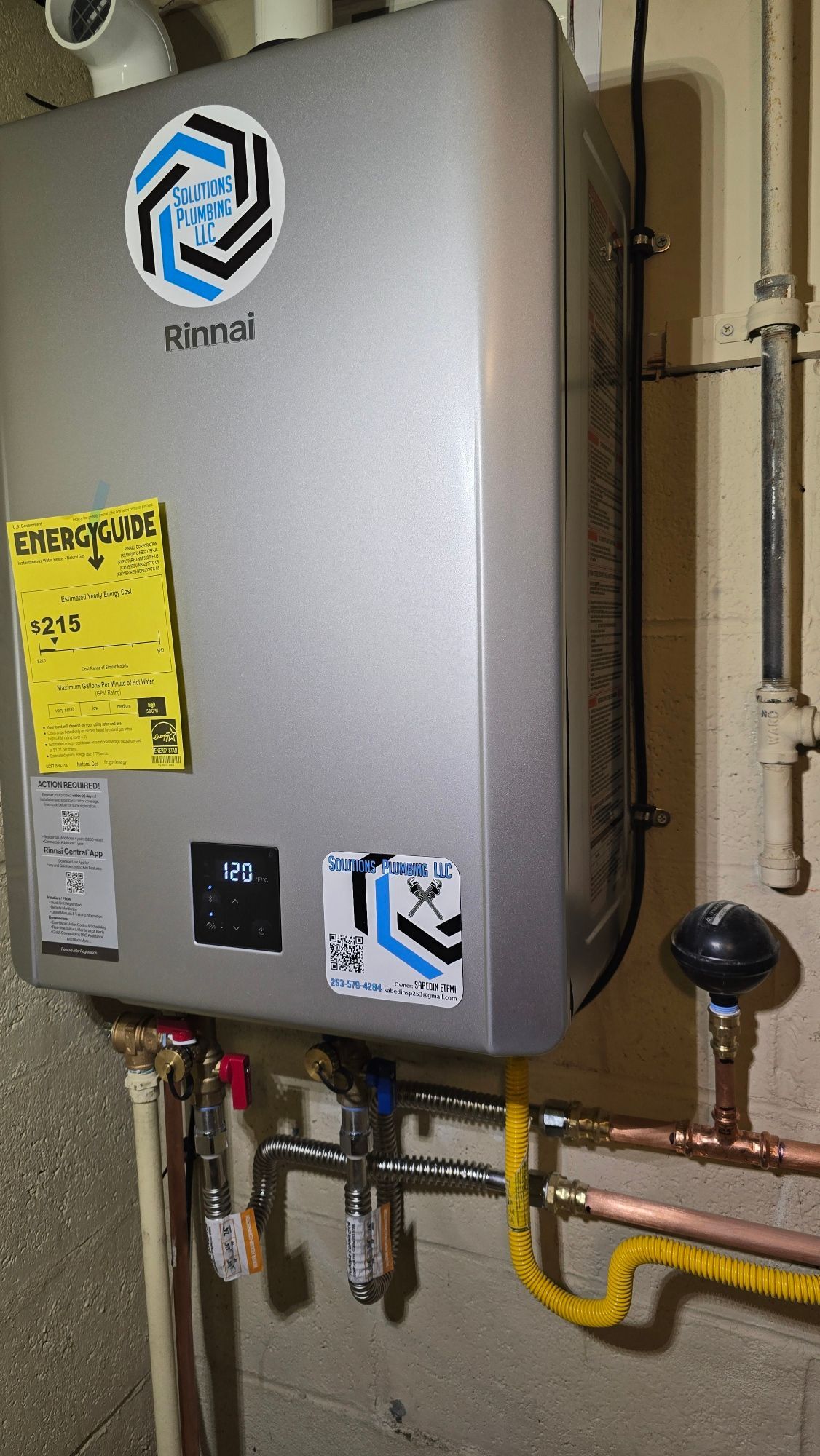 A silver Rinnai tankless water heater installed on a wall with various pipes connected to it.