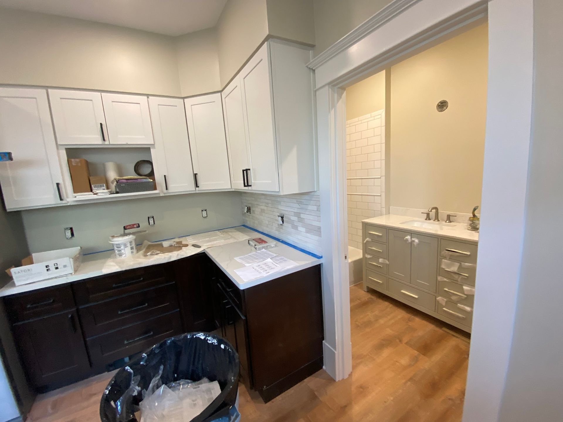 Kitchen and bathroom under renovation; white and dark brown cabinets, light-colored walls, open doorway.