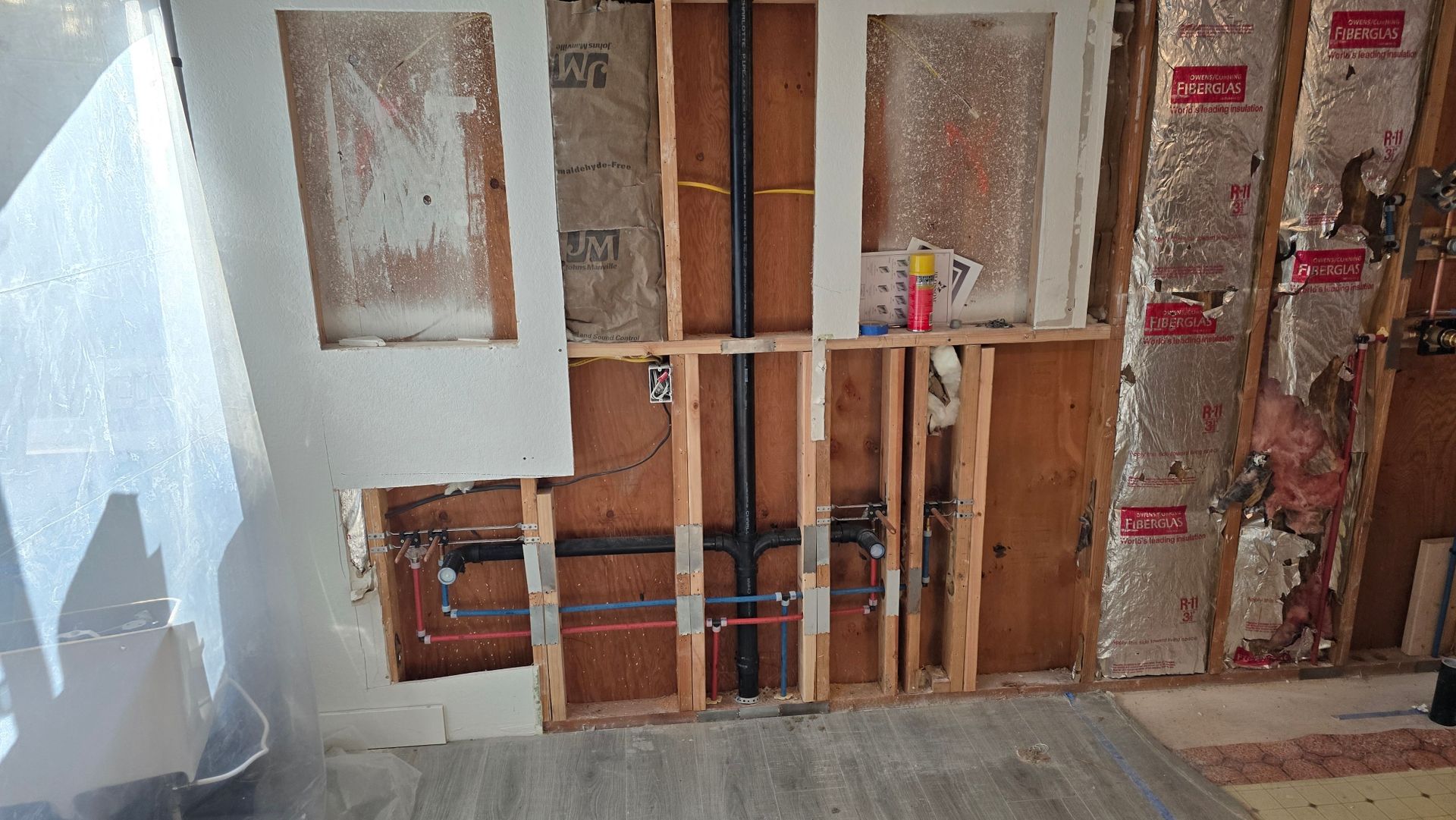 Interior wall under construction showing exposed framing, insulation, and plumbing.
