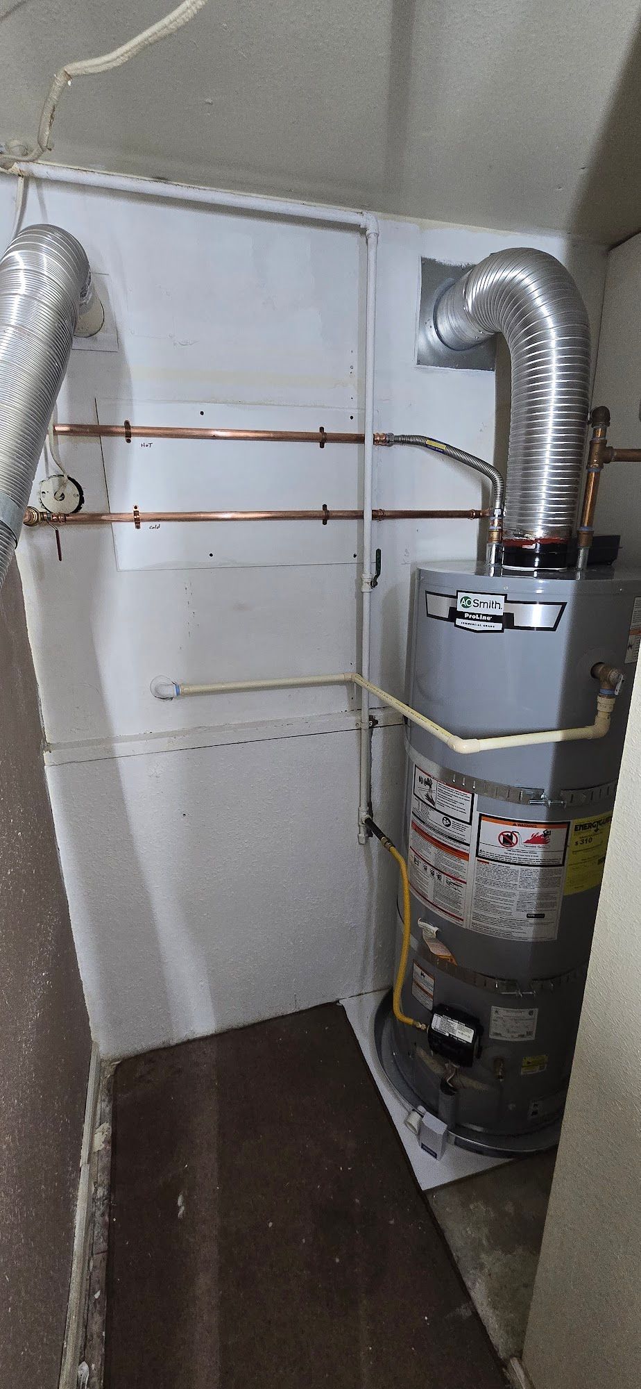 A water heater installed in a corner. Copper pipes and metal ductwork visible.