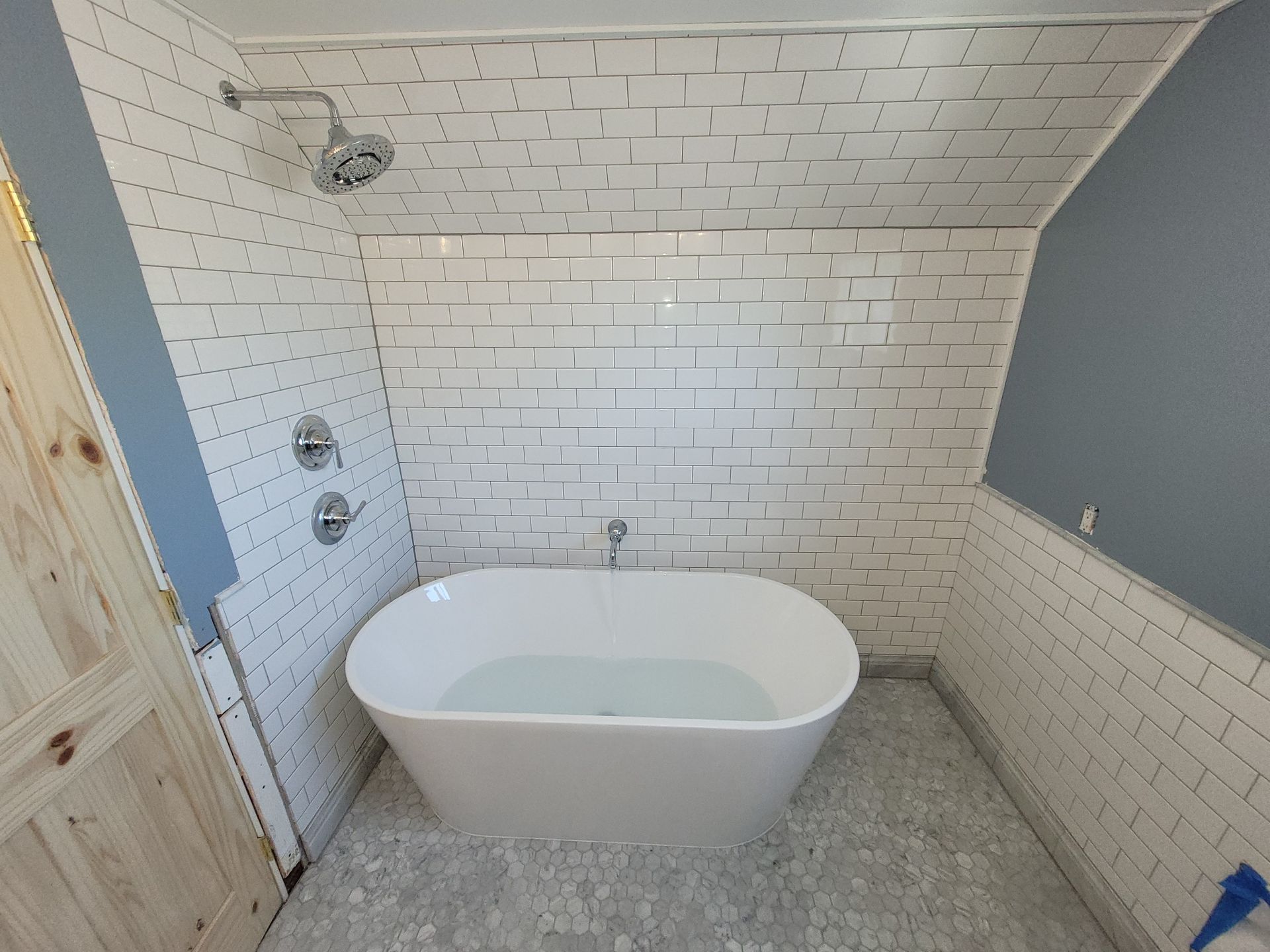 White tiled bathroom with oval soaking tub, showerhead, and blue walls.