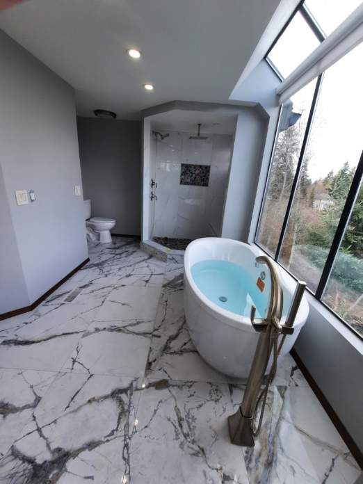 Luxury bathroom with white marble floor, freestanding tub, walk-in shower, and large windows.