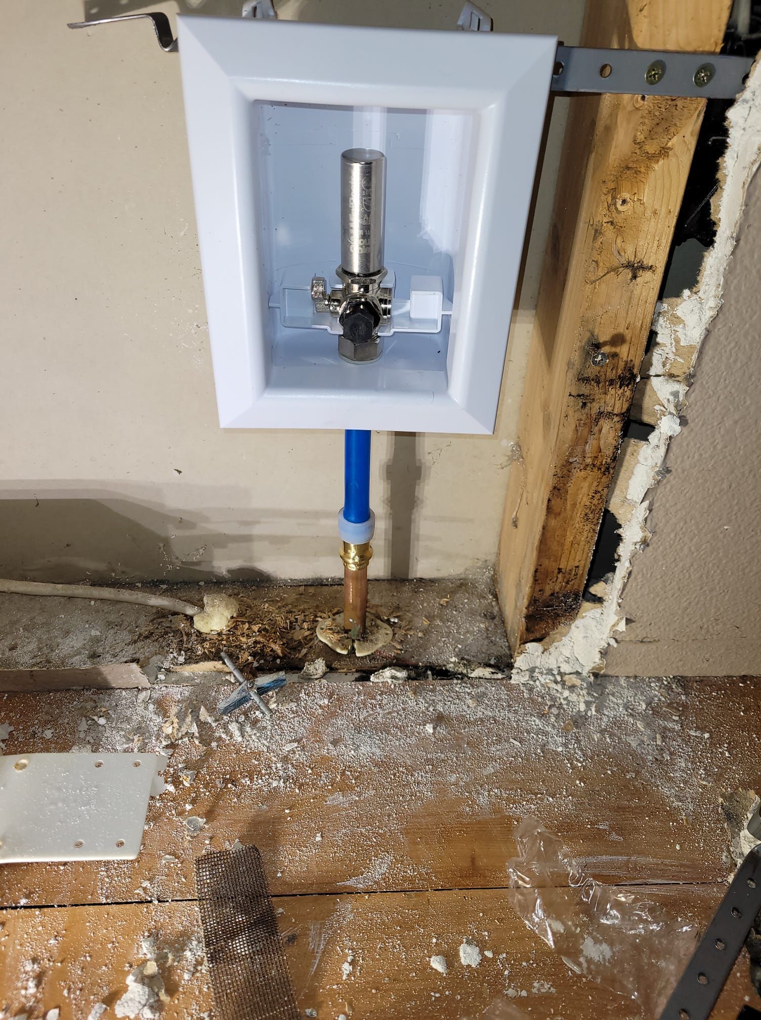 White laundry box with water supply pipes against a wall and wooden framing.