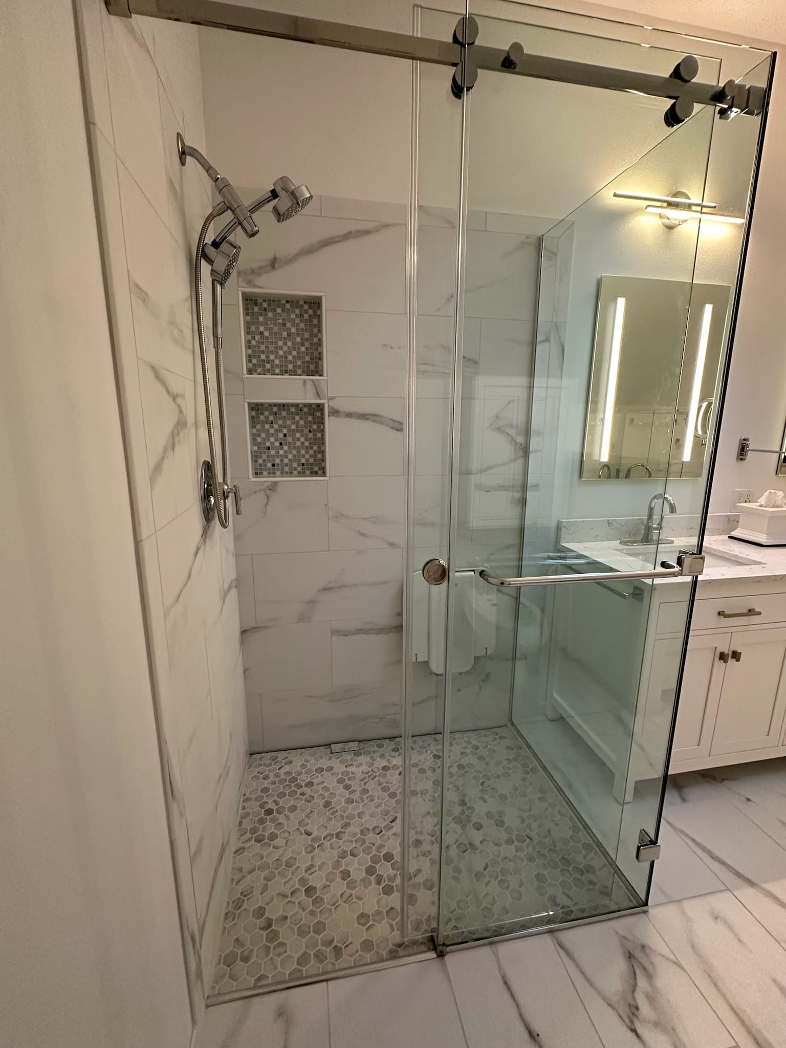 Modern glass shower with marble tile walls, pebble floor, and sliding door.