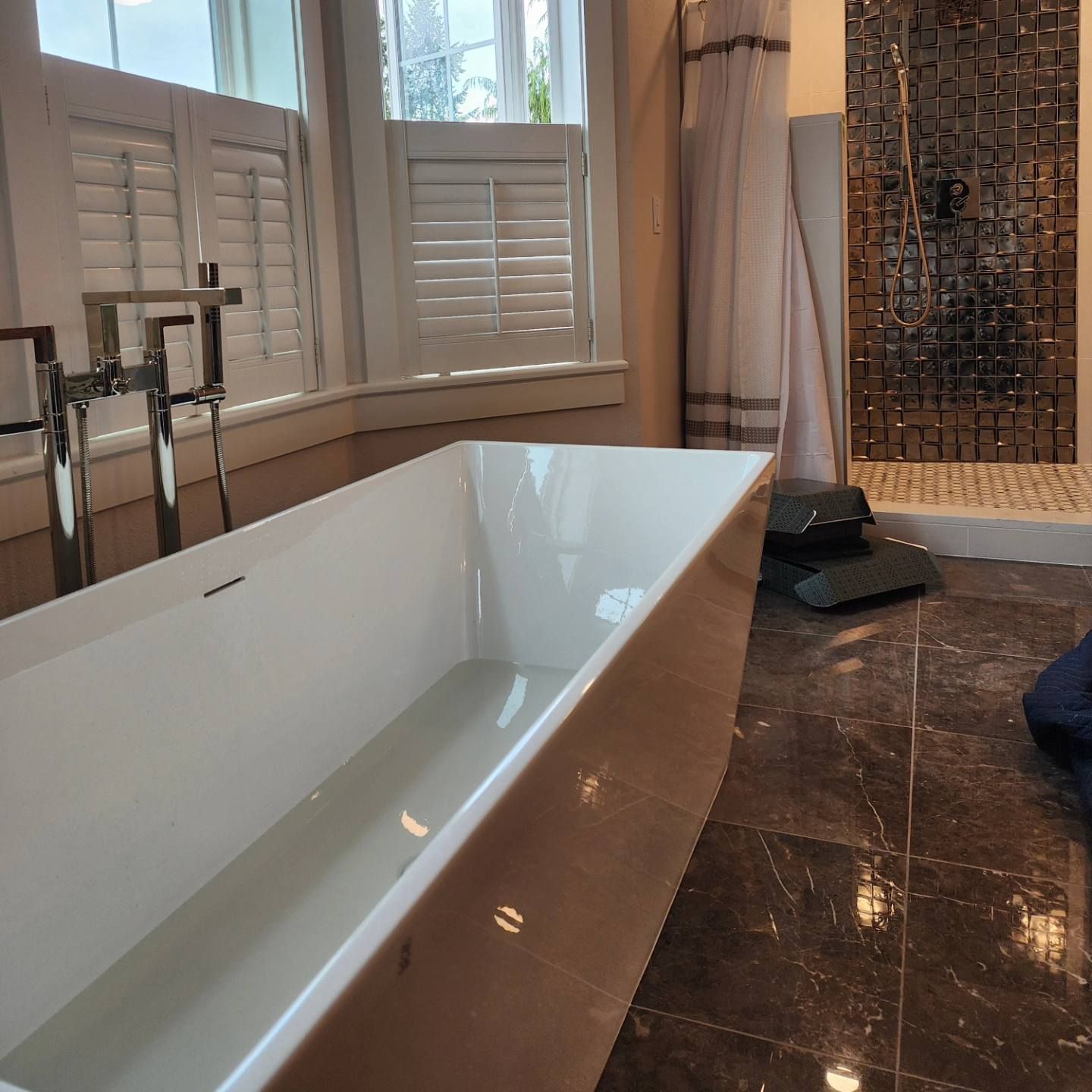 Modern bathroom with a white rectangular bathtub, shower, and window with shutters.