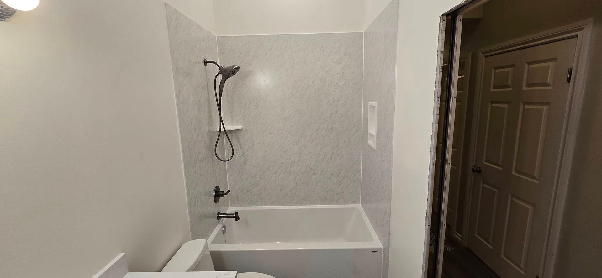 Bathroom with a white bathtub, shower fixtures, and light-colored walls and door.