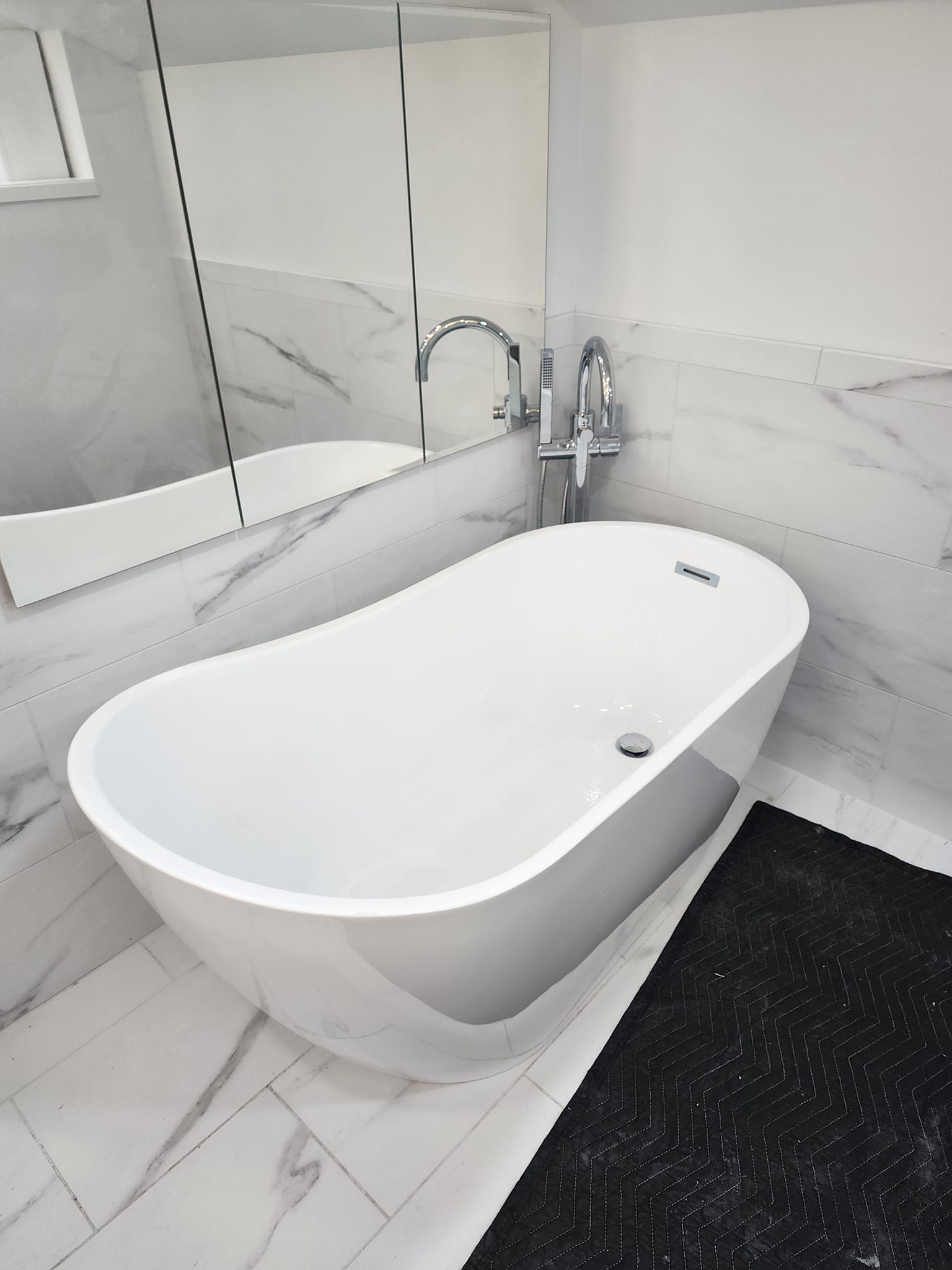 White oval bathtub in a modern bathroom with marble tile and chrome fixtures.