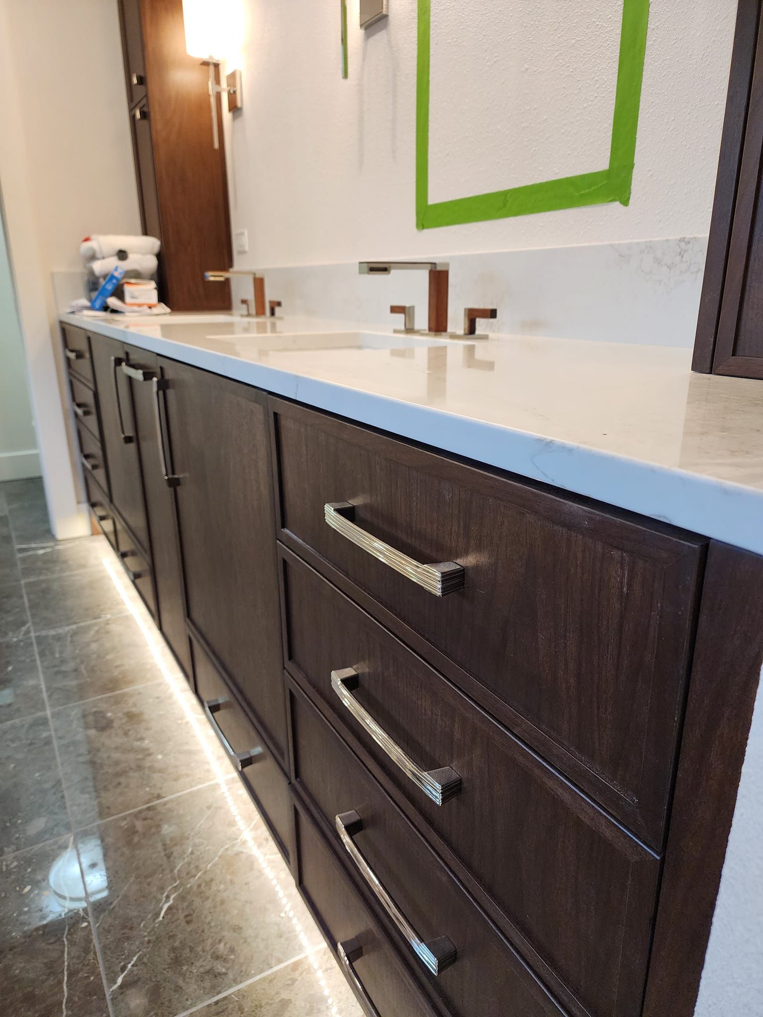 Dark wood bathroom vanity with drawers and silver handles. Countertop with faucet and under-cabinet lighting.