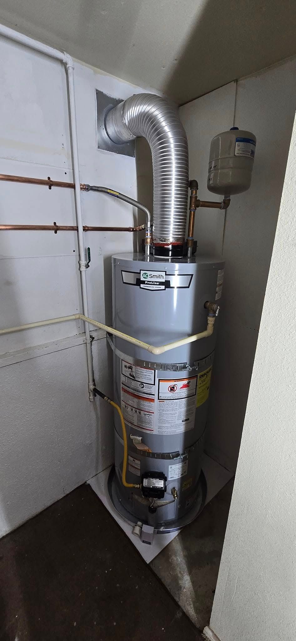 A water heater in a corner, with vent pipe and copper pipes.