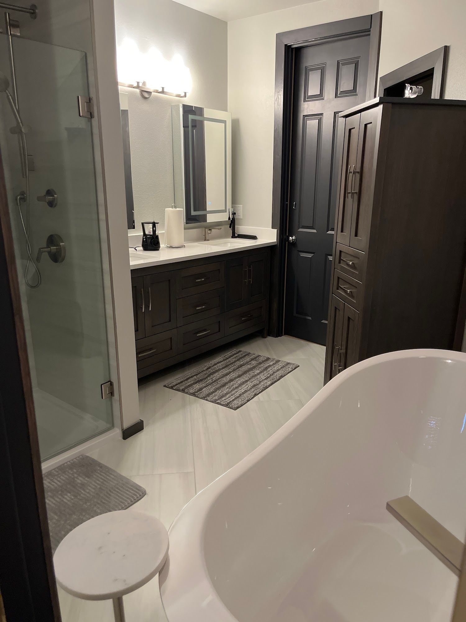 Bathroom with a white bathtub, dark cabinets, a shower, and a dark door.