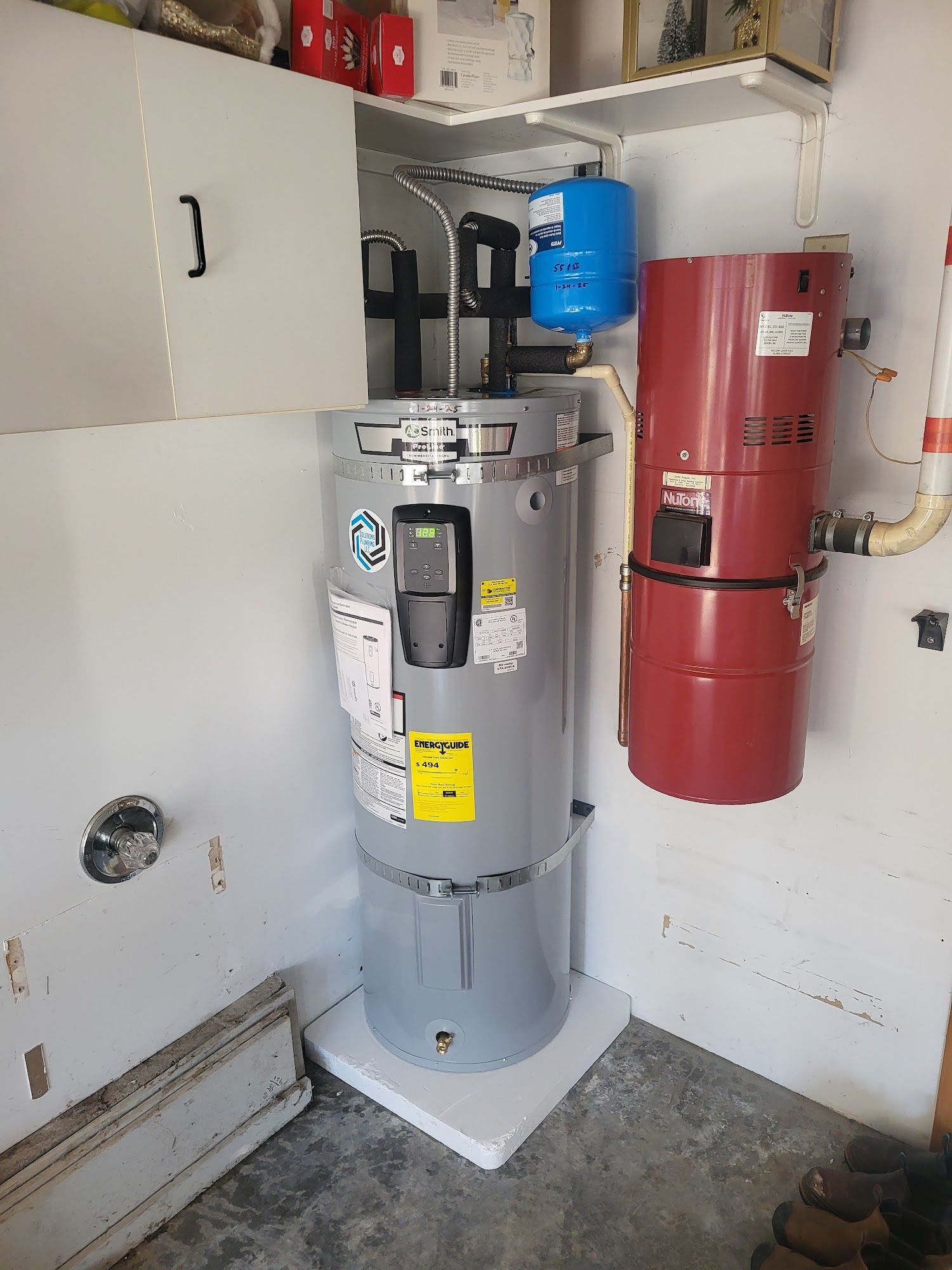 A water heater and a hot water recirculation pump are in a corner of a garage. The water heater is gray.