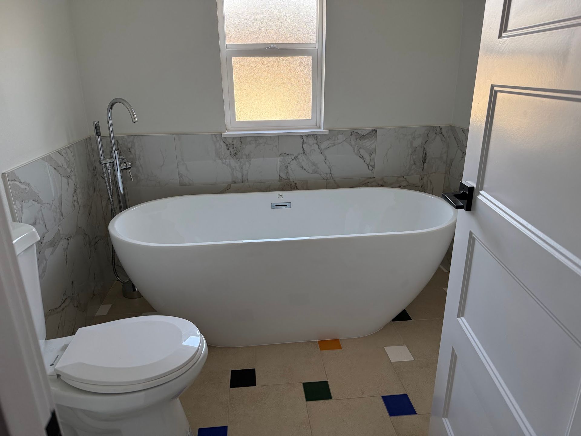 White bathtub and toilet in a bathroom with patterned tile and marble-look wall tile.