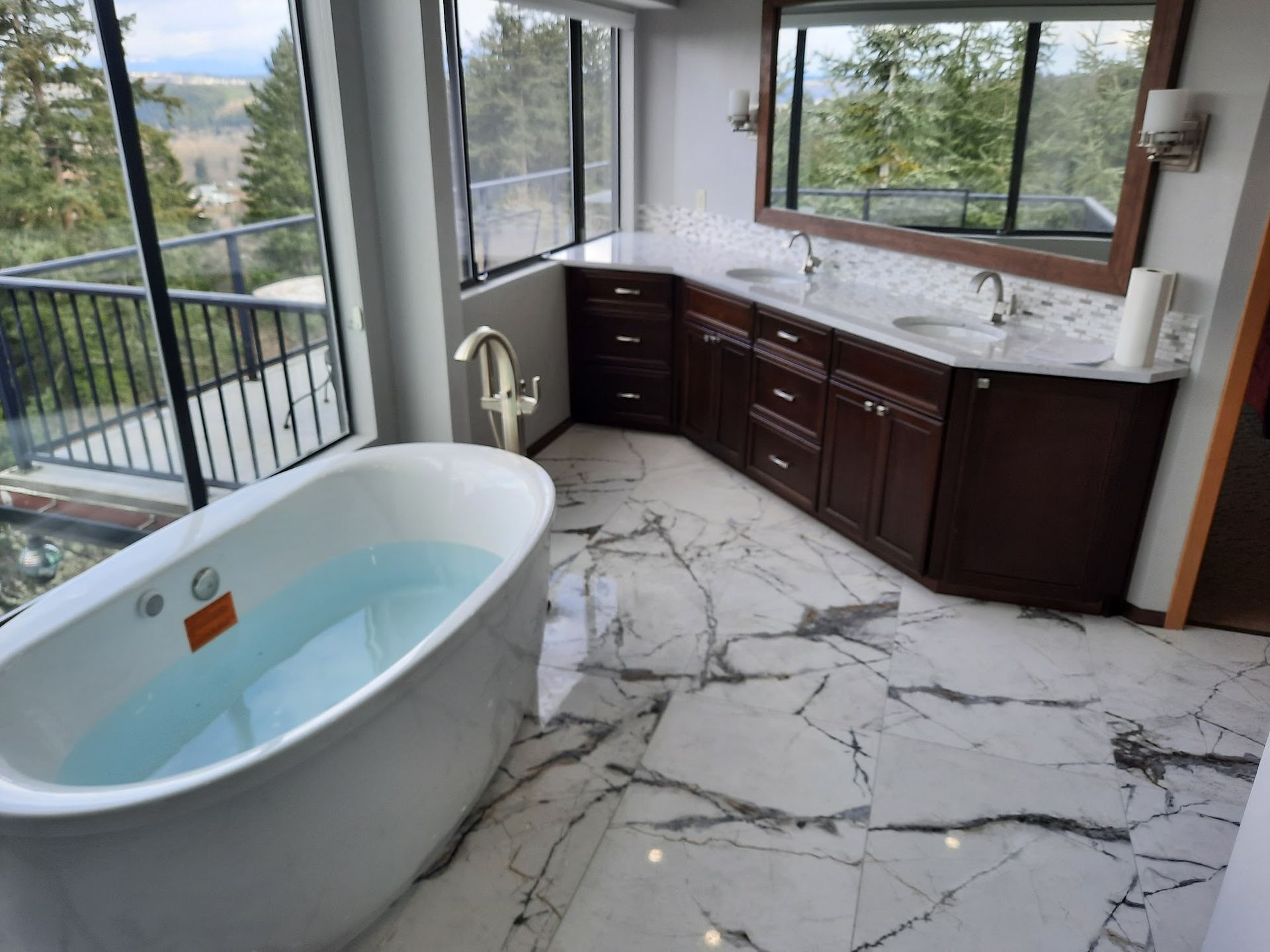 Bathroom with a freestanding tub, dark wood vanity, and marble tile flooring. Windows offer an outdoor view.