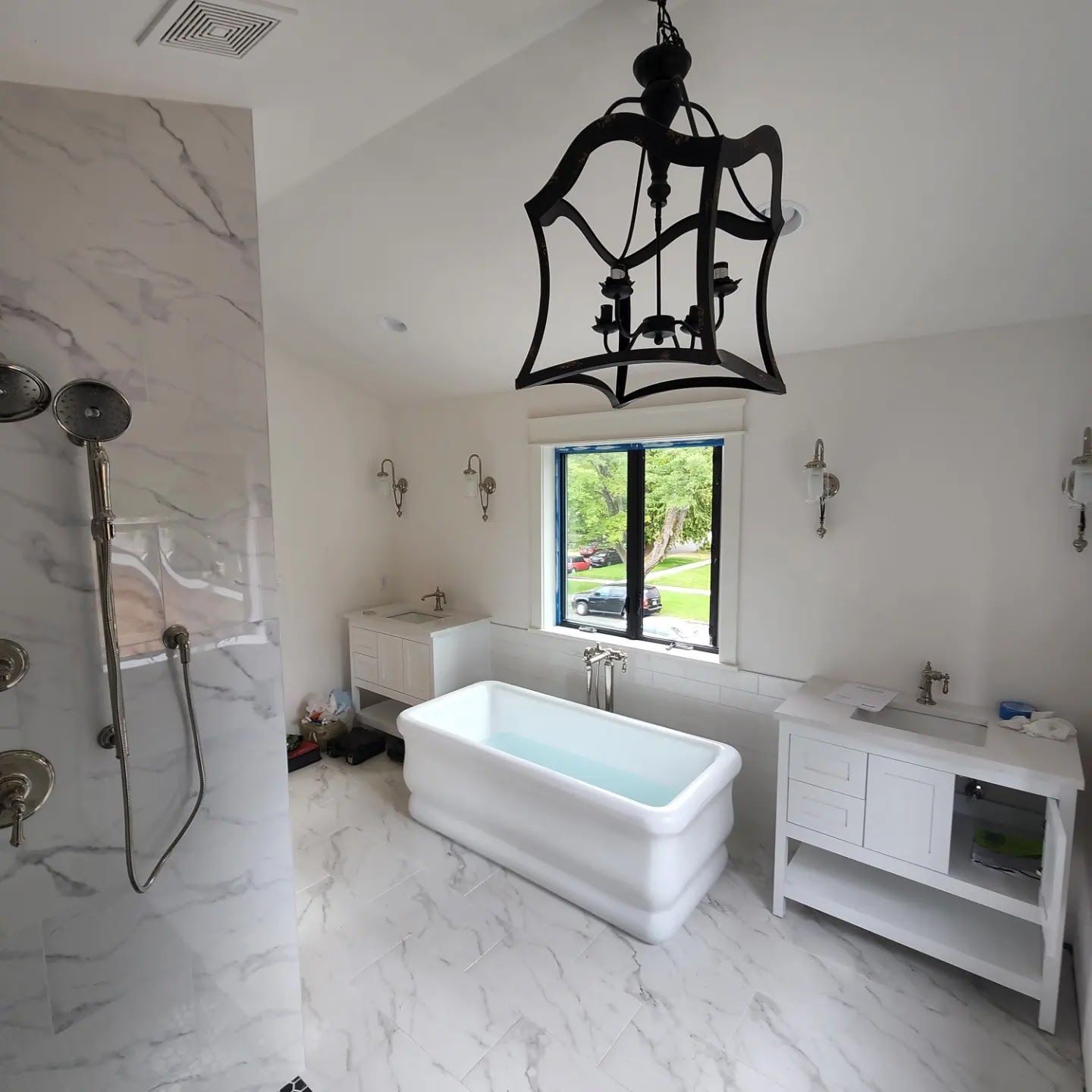 Luxurious white marble bathroom with a freestanding tub, dual vanities, and a black chandelier.