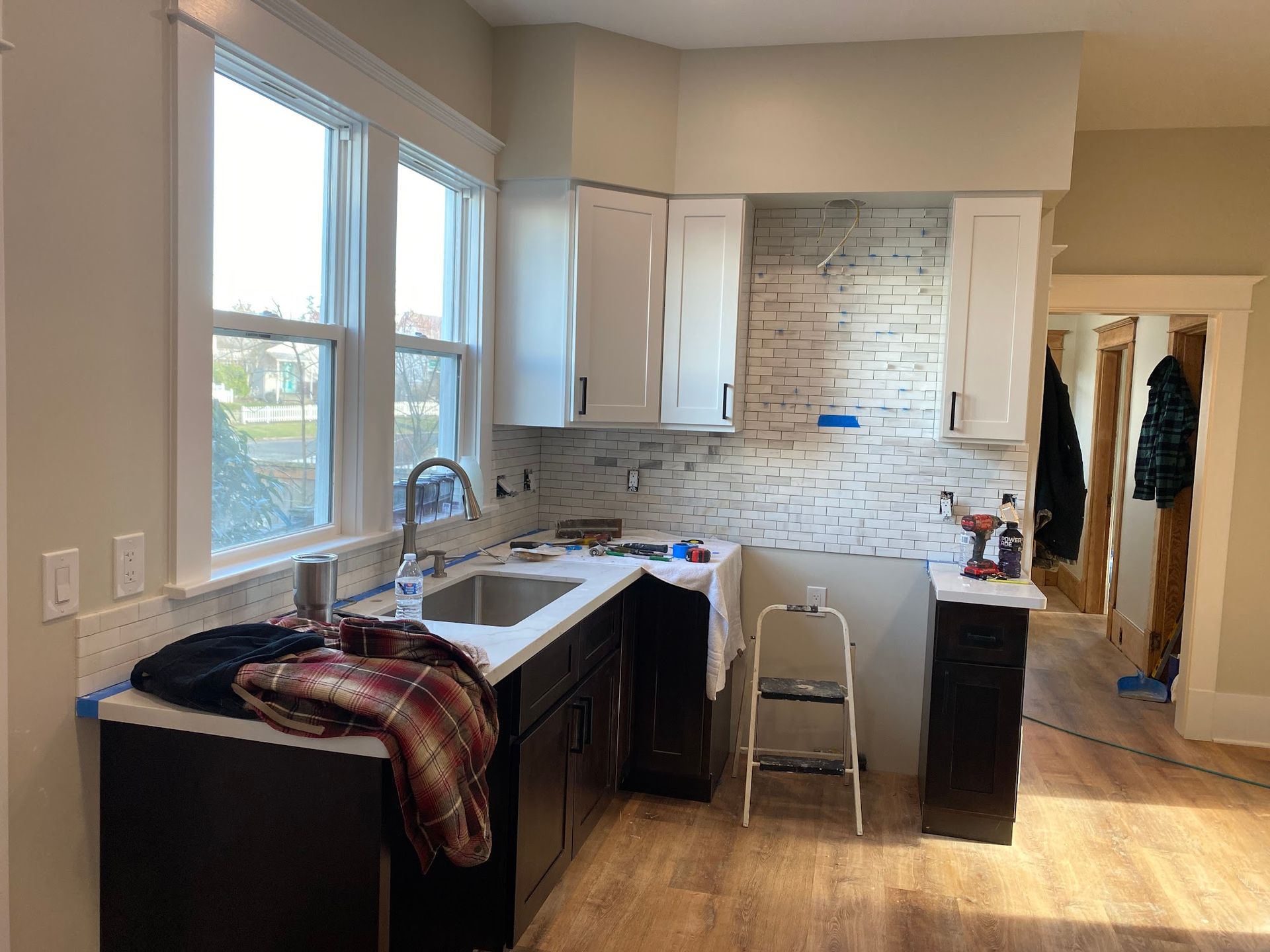Kitchen renovation in progress: white cabinets, dark counters, sink, brick backsplash, and a step stool.