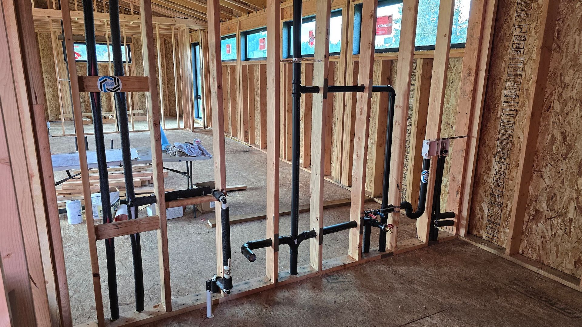 Interior of a building under construction, showing black plumbing pipes within wood framing.