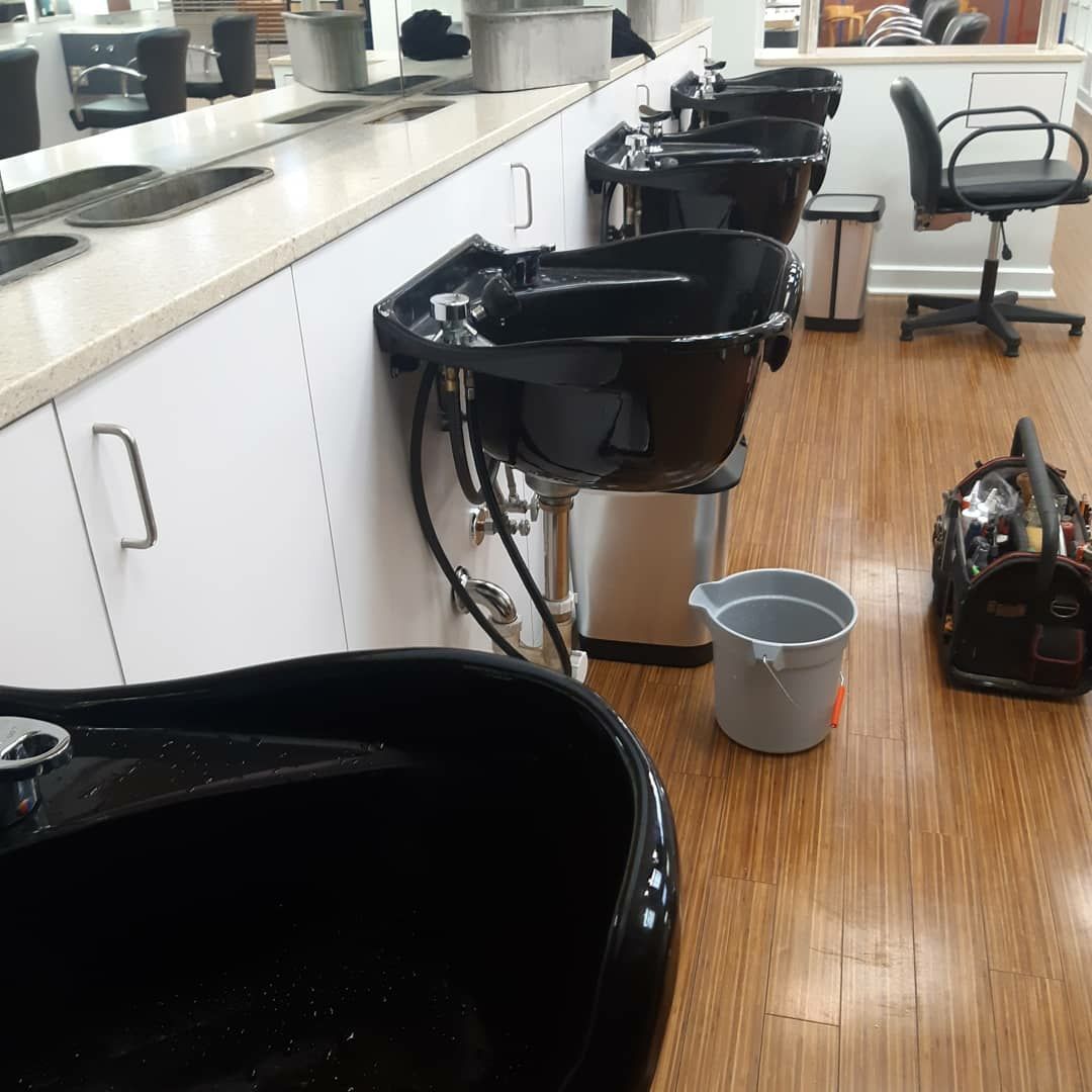 Hair salon interior with several black shampoo bowls, a gray bucket, and a rolling chair.