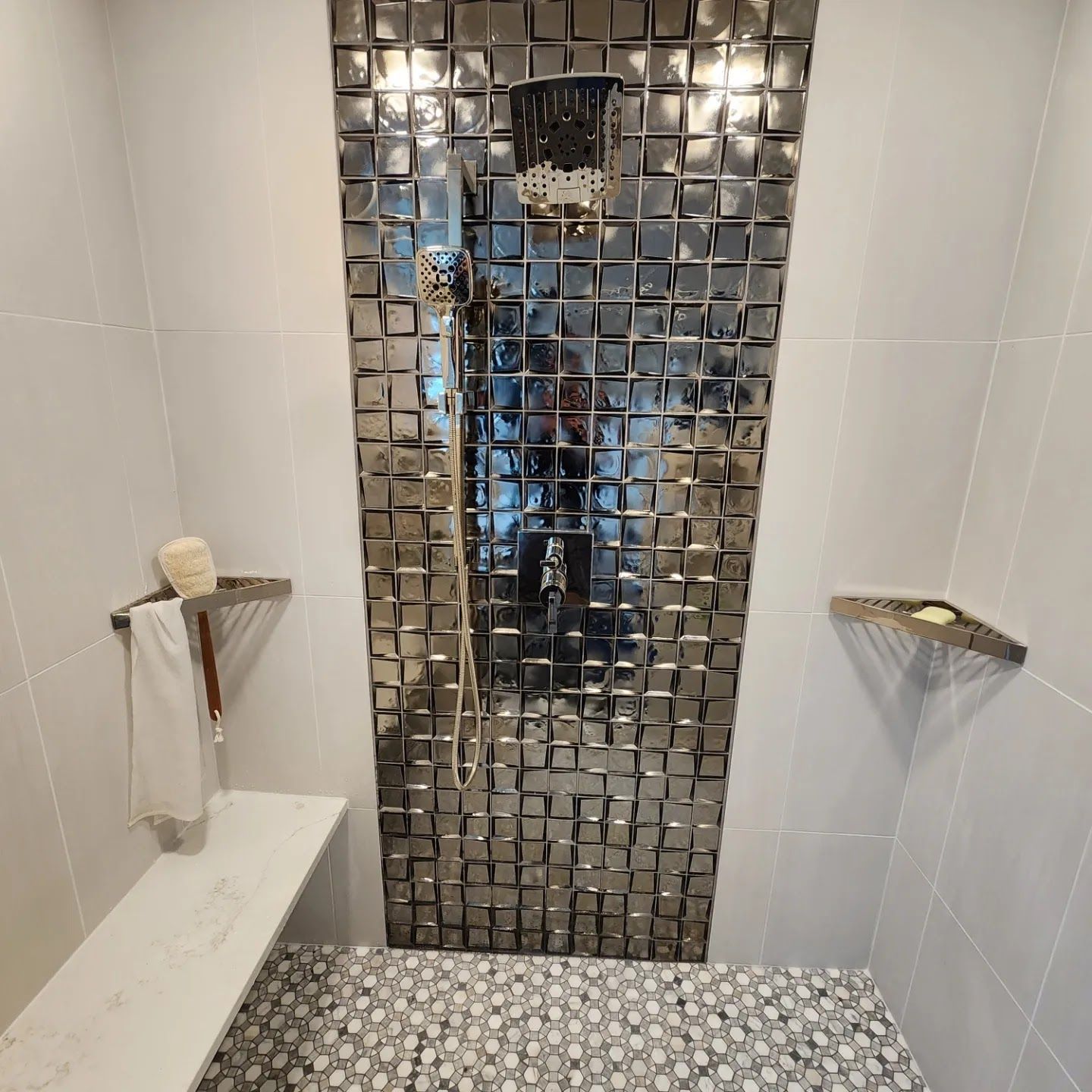 Shower with silver tile accent wall, bench, pebble floor, and stainless steel fixtures.