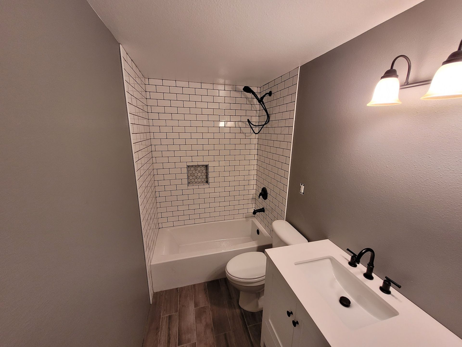 Bathroom with white brick tile shower, white sink, and black fixtures.