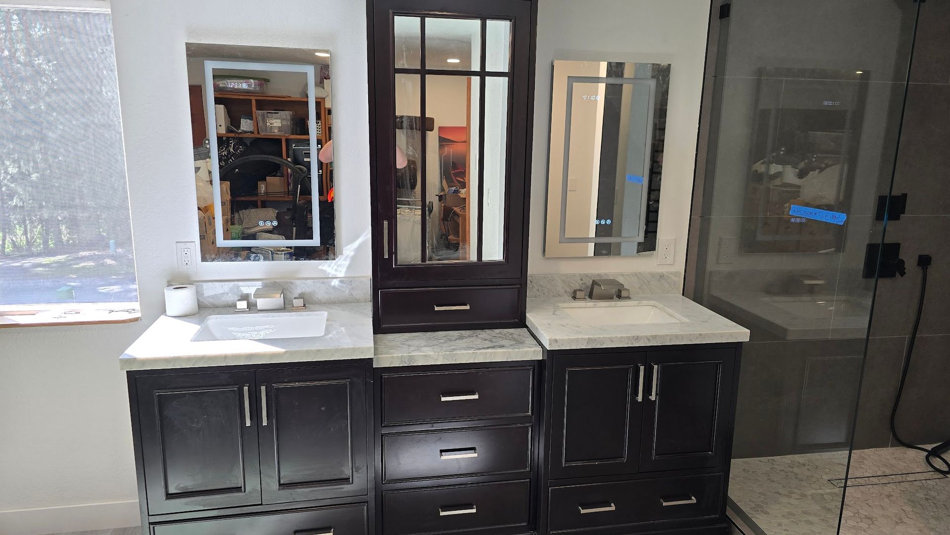 Bathroom vanities with dark cabinets and light countertops, mirrors, and a tall cabinet.
