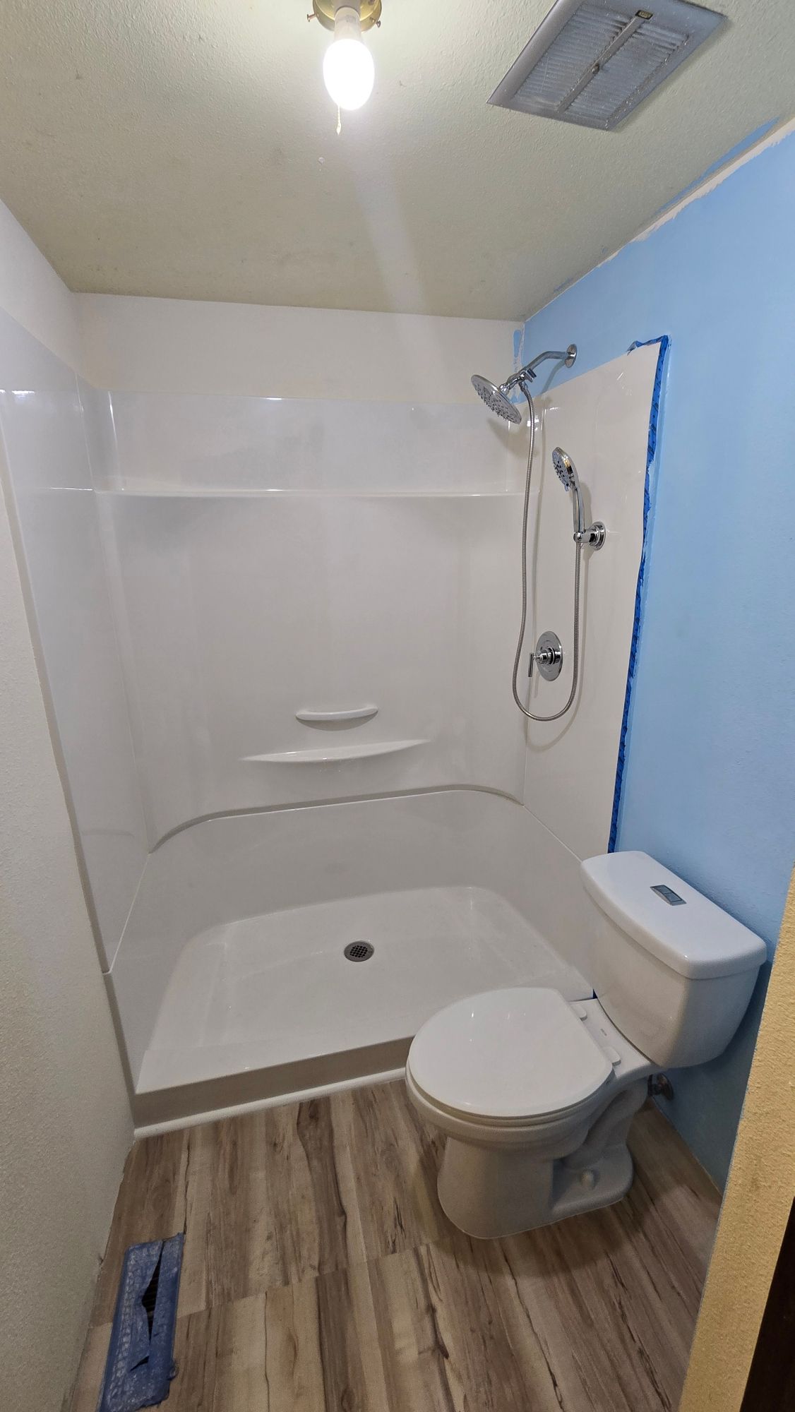 White shower stall and toilet in a bathroom with blue wall, wood-look floor, and silver shower fixtures.