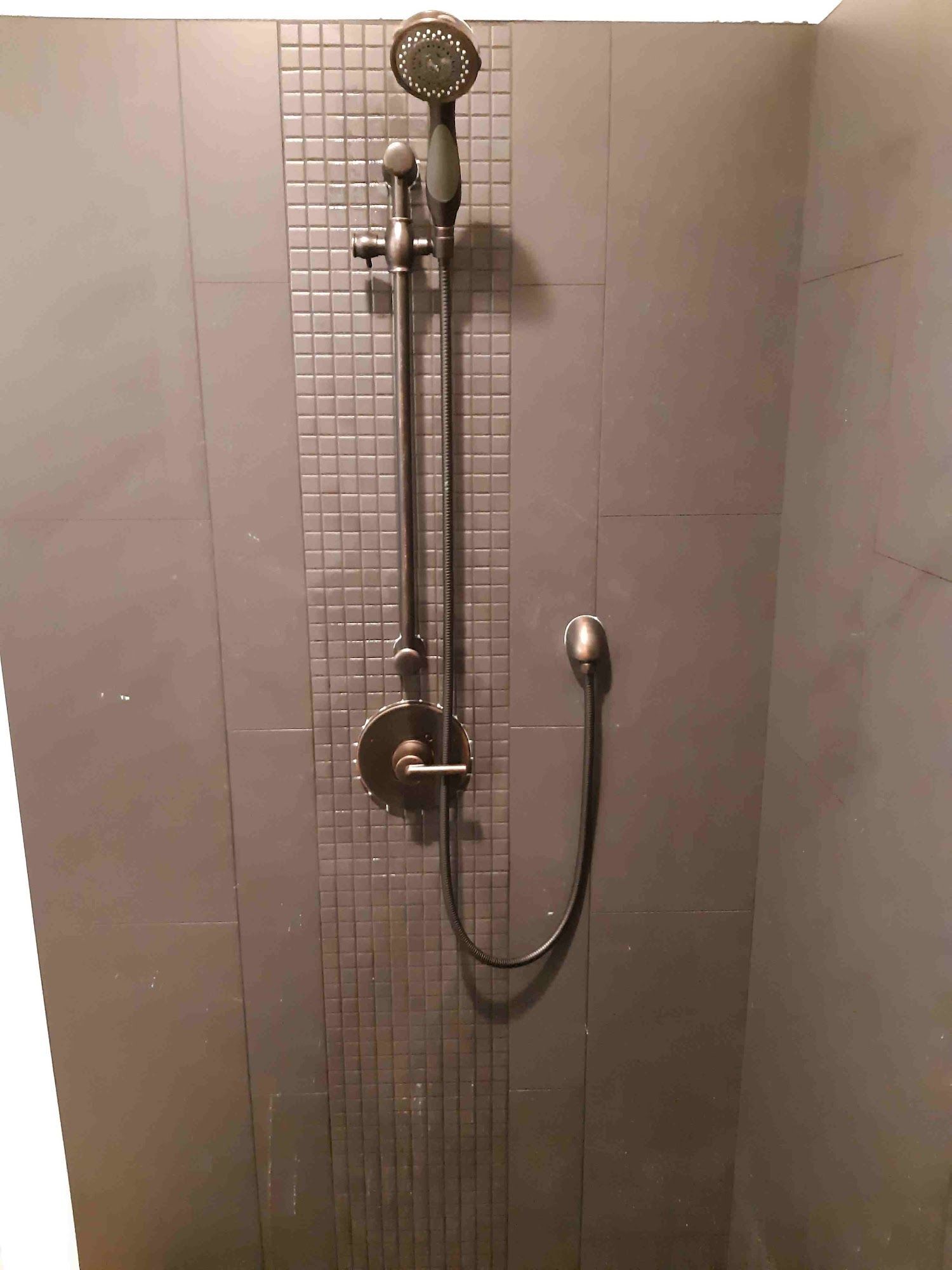 Shower with silver fixtures on gray tiled wall.