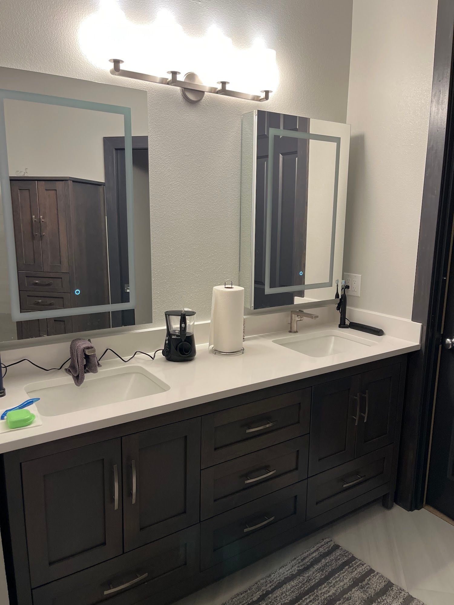 Dark wood double vanity with white countertop, two mirrors, and overhead lighting.