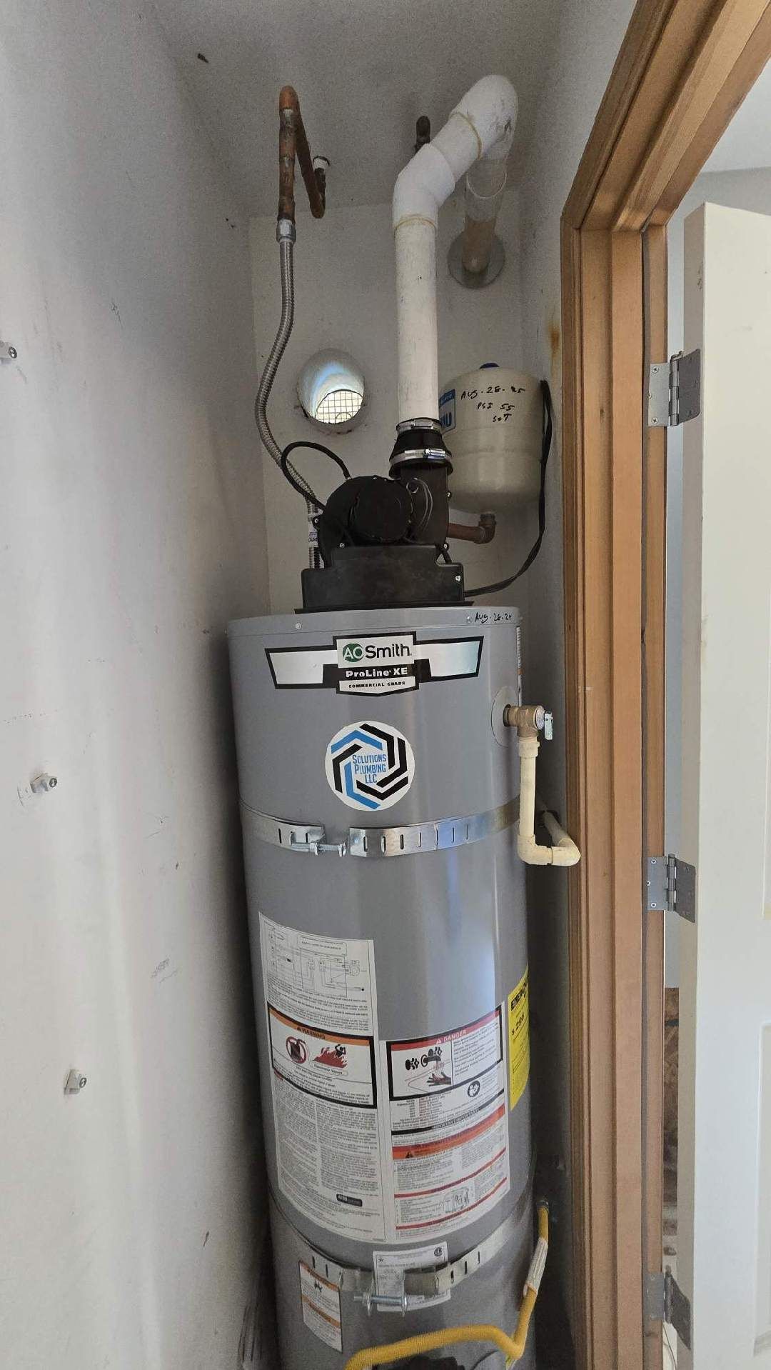 Water heater in a small, enclosed space with vent pipe, pipes, and controls.