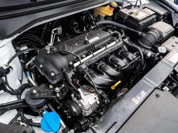 Car engine bay, black engine with various components, white car, setting is outdoors. | Automotive Excellence
