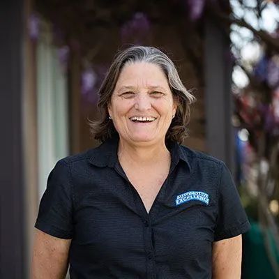Woman in black shirt smiling, outdoors. Purple flowers in the background. | Automotive Excellence