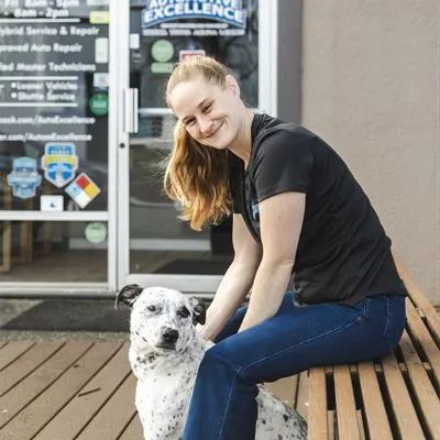 Woman with dog sits outside auto repair shop. | Automotive Excellence