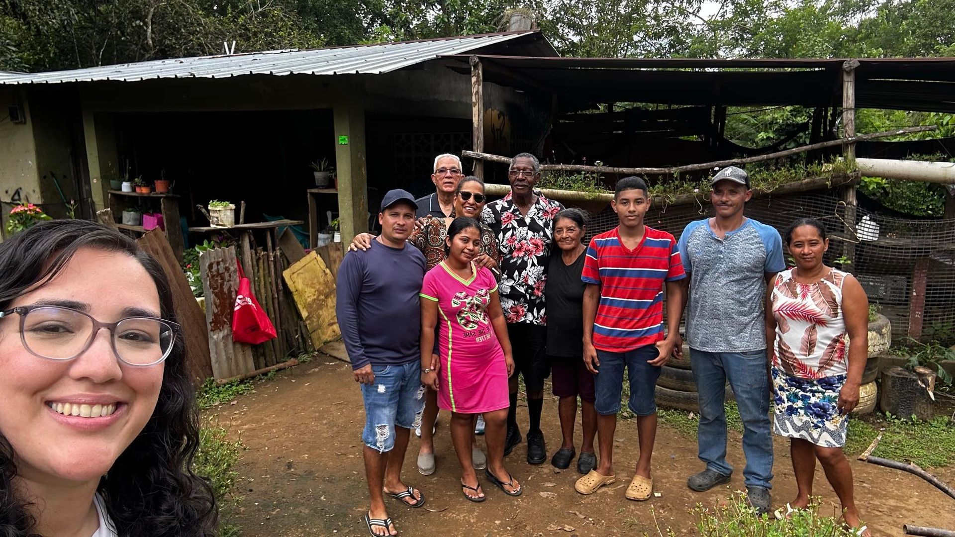 Group of diverse people smiling in front of a house, outdoors. One person taking selfie.