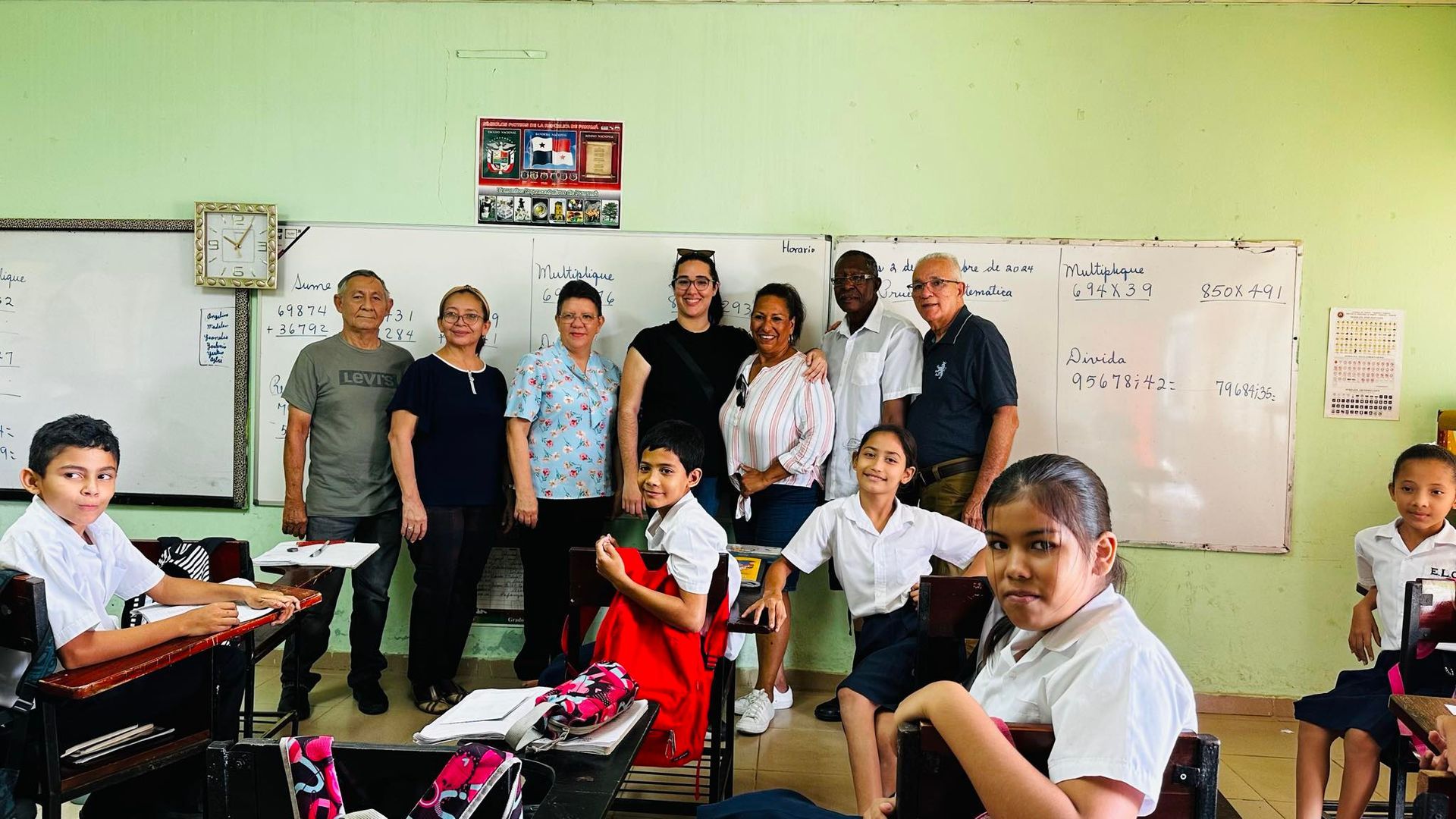 Group of adults and students in a classroom, posing near a whiteboard.