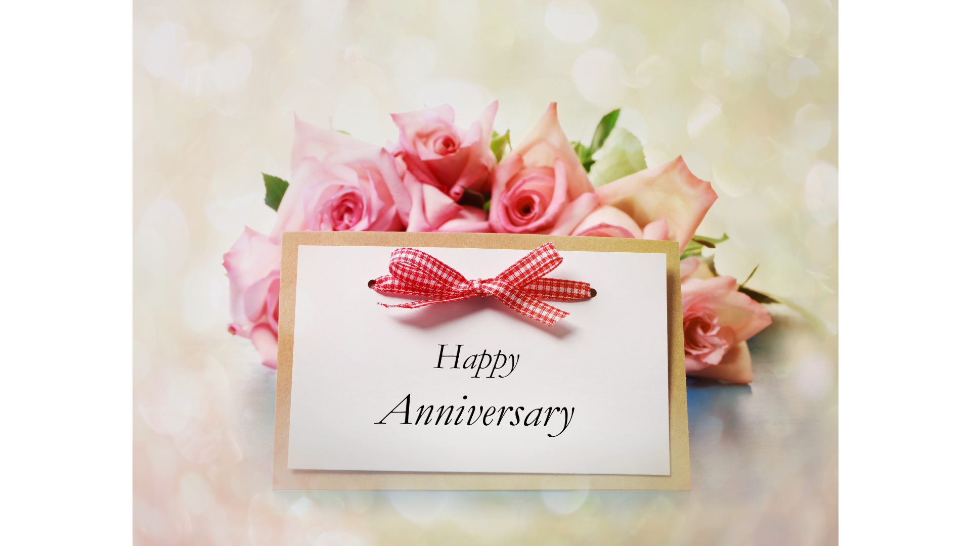 A happy anniversary card is sitting next to a bouquet of pink roses.