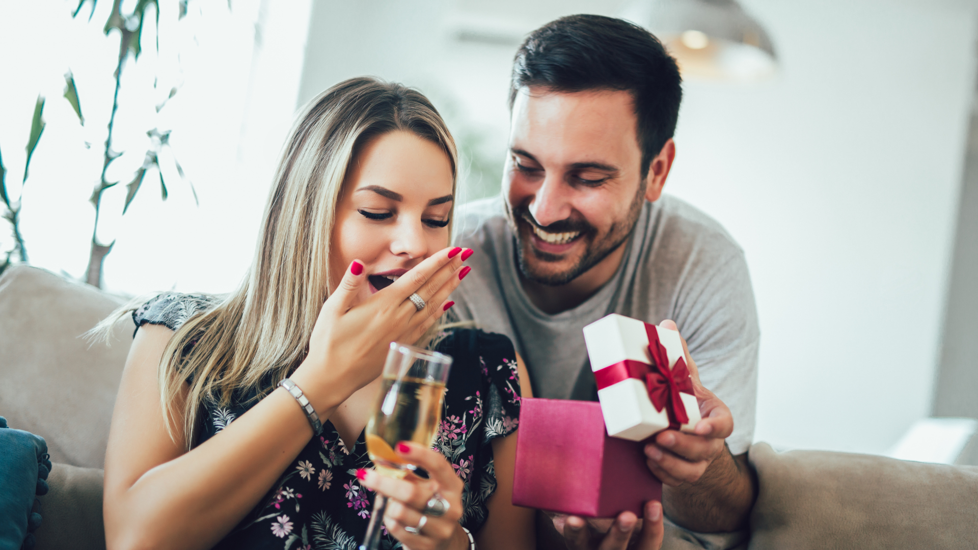 A man is giving a gift to a woman while they are sitting on a couch.