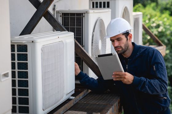 A man is looking at a tablet while standing next to an air conditioner.
