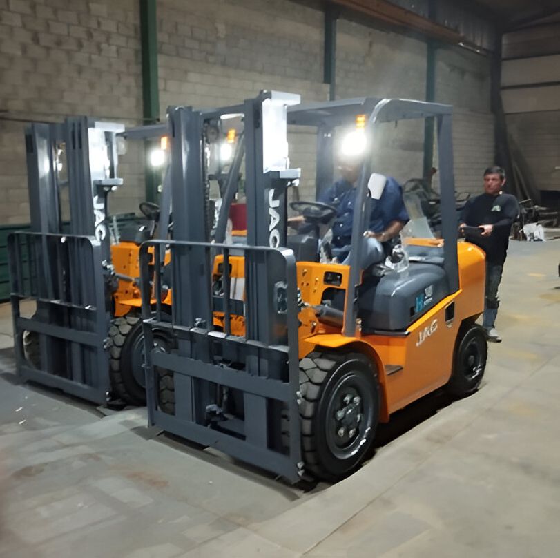 Tres carretillas elevadoras de color naranja en un almacén, una con conductor y otra persona cerca.