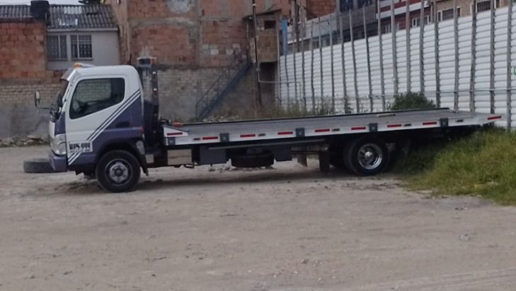 Grúa estacionada sobre grava al lado de un terraplén cubierto de hierba y una valla blanca.